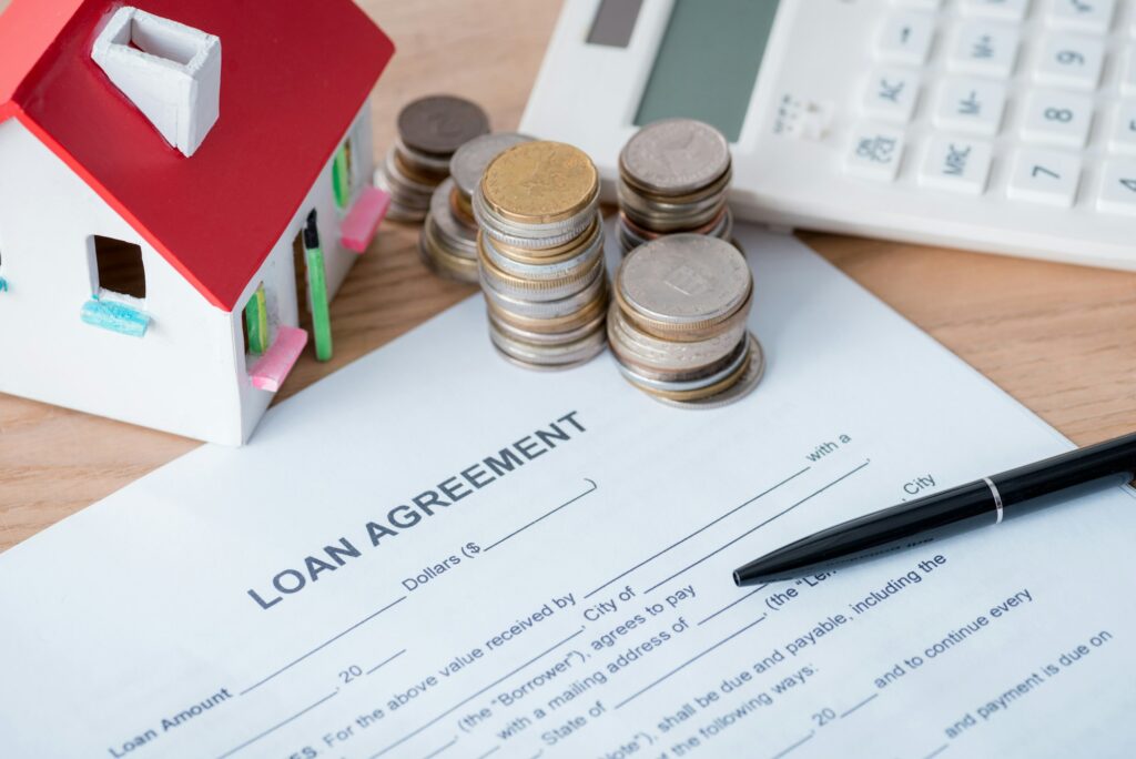 loan agreement, house model, calculator, silver and golden coins on wooden surface